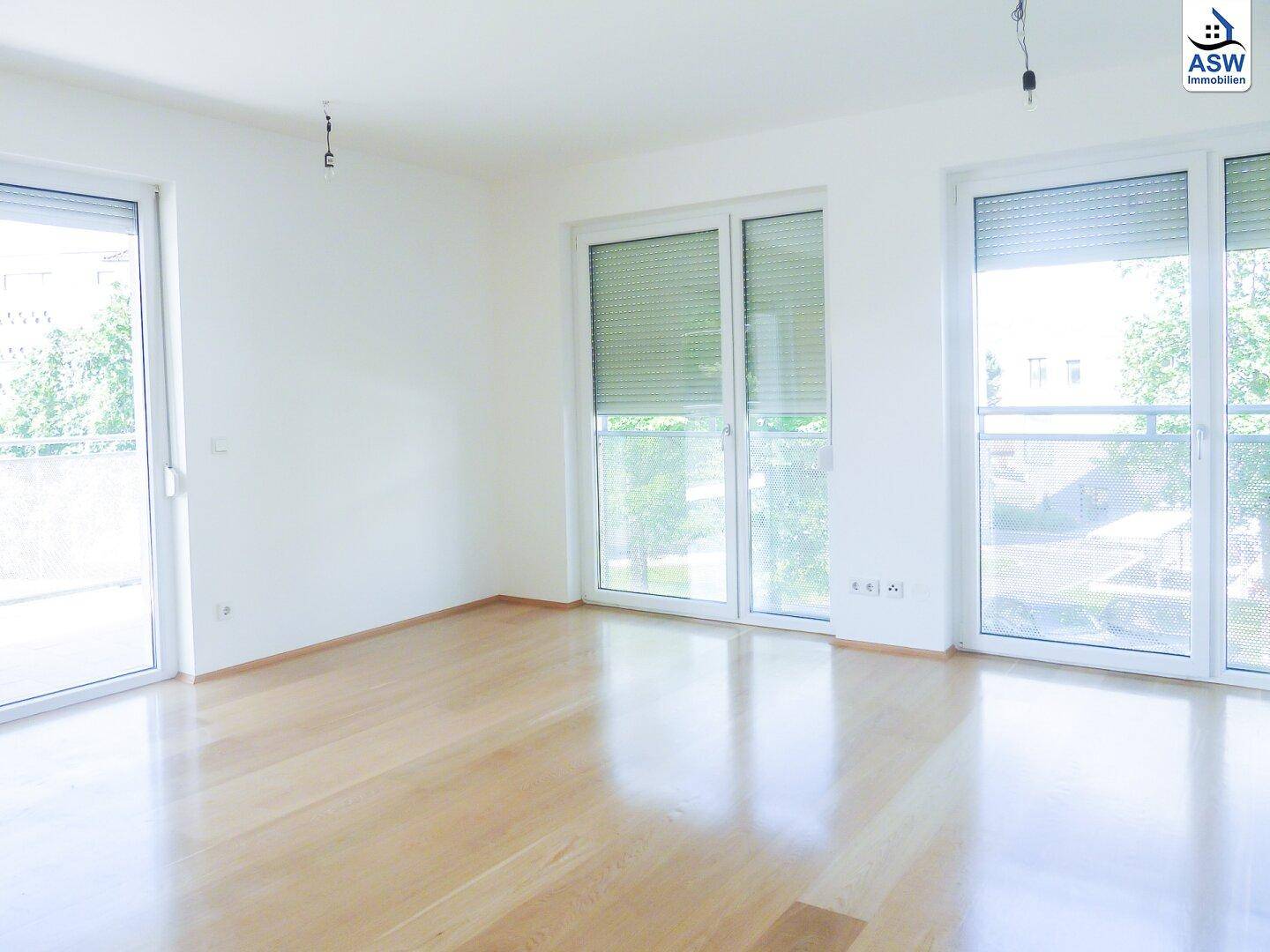 Heller Wohnraum mit glänzendem Parkettboden und großen Fenstern, die viel Tageslicht hereinlassen.