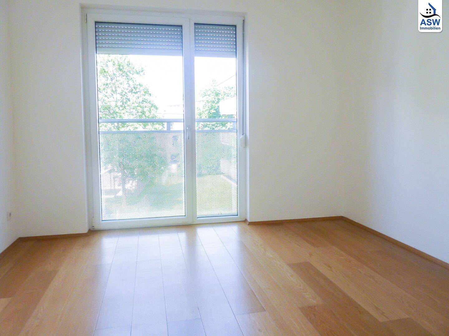 Freundliches Zimmer mit Parkettboden und großem Fenster, das einen Blick ins Grüne bietet.
