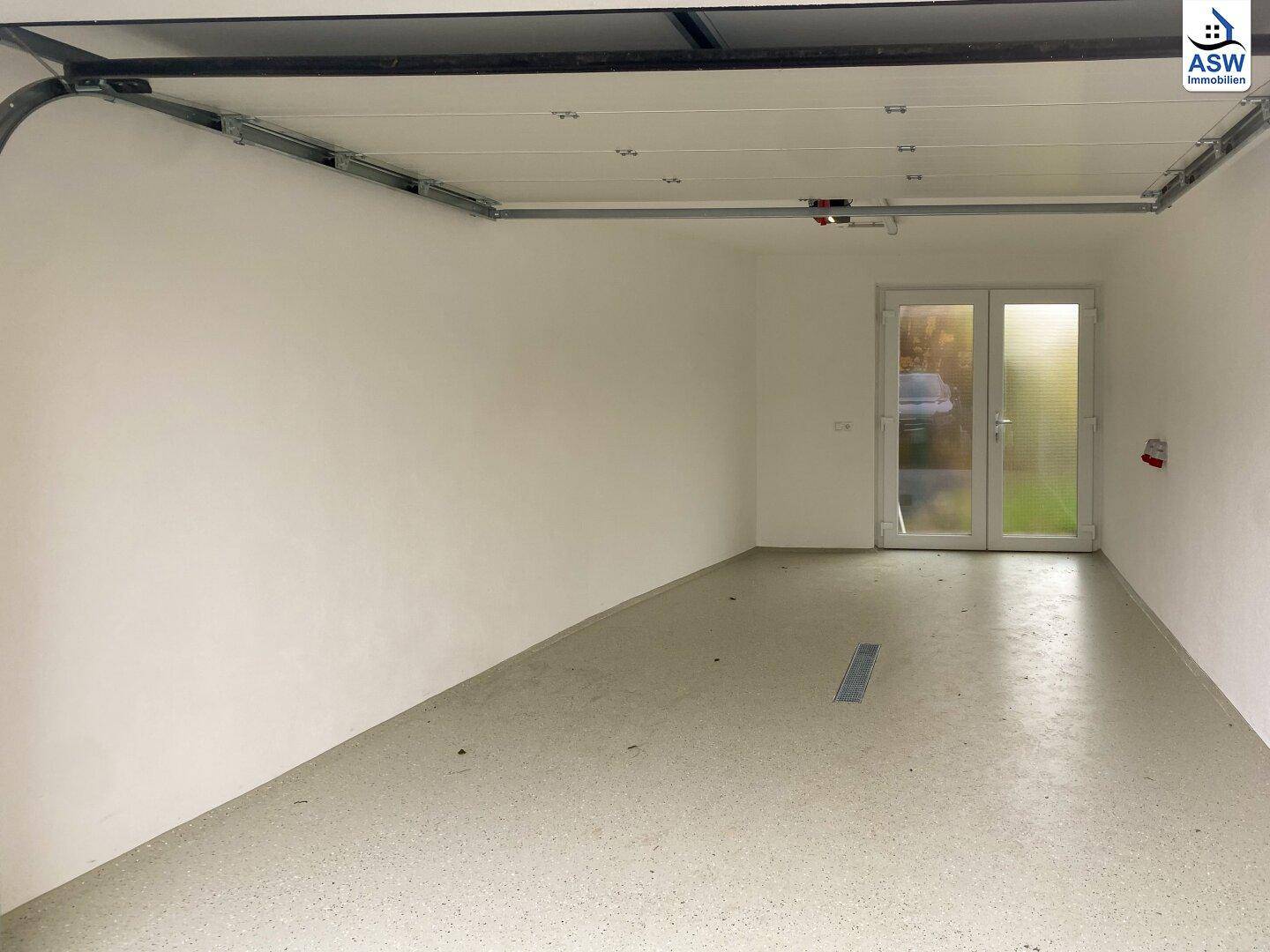 Geräumige Garage mit automatischem Tor und Zugangstür zum Gartenbereich.