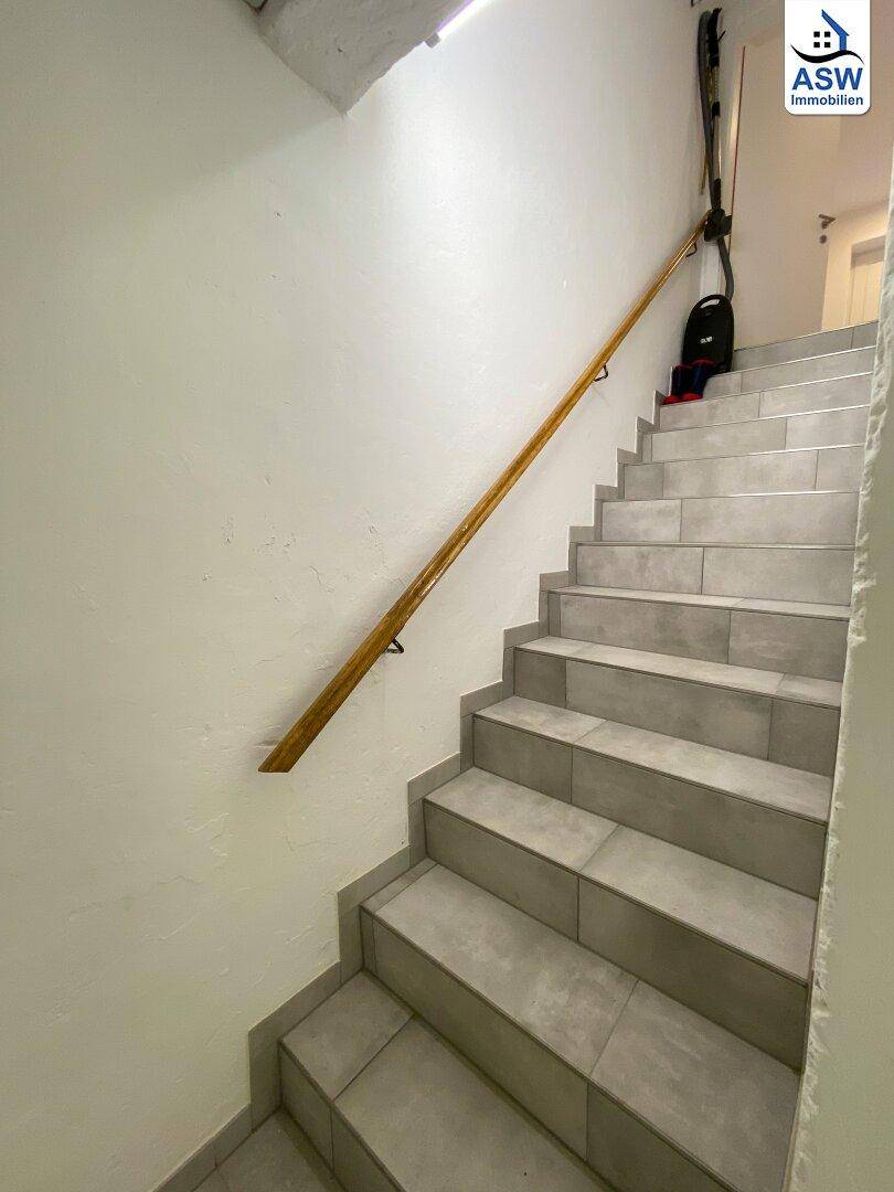 Heller Treppenaufgang mit Fliesenboden und Holzhandlauf, der in die oberen Etagen führt.