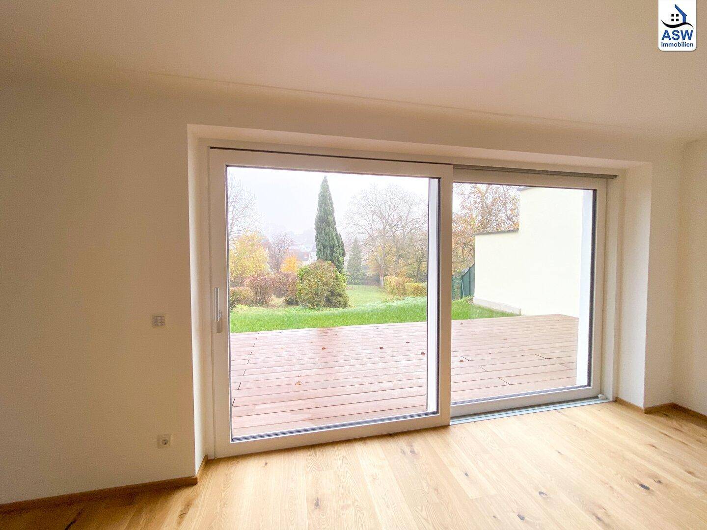 Heller Raum mit großem Schiebefenster, Holzboden und Blick auf die Terrasse und den Garten.