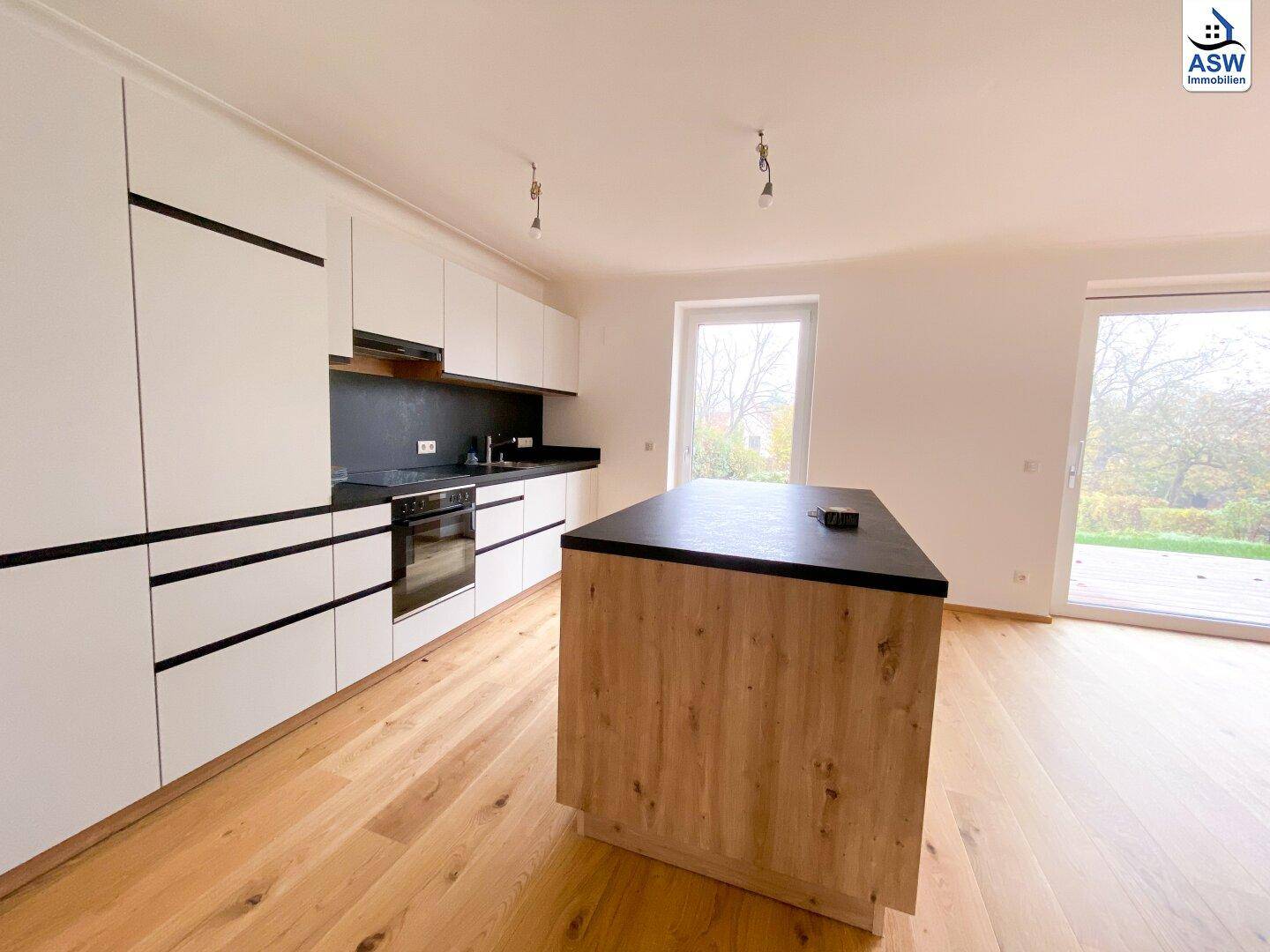 Moderne Einbauküche mit Kücheninsel, weißen Fronten und dunkler Arbeitsplatte auf Holzparkett.