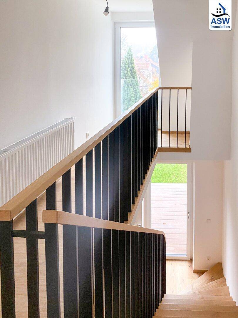 Moderne Holztreppe mit schwarzem Geländer und großem Fenster mit Blick ins Grüne.