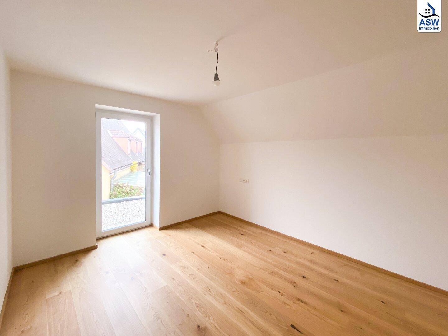 Gemütliches Schlafzimmer im Dachgeschoss mit Eichenparkett und Zugang zu einem Balkon.