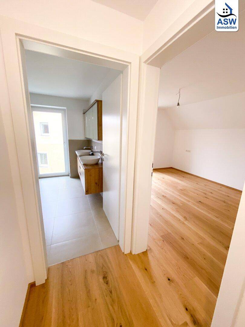 Heller Flur mit Blick auf das Badezimmer und ein weiteres Zimmer mit Holzboden.