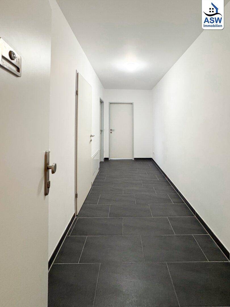 Heller Flur mit dunklem Fliesenboden und weißen Wänden, der zu verschiedenen Zimmern führt.