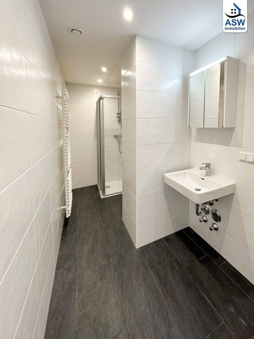 Modernes Badezimmer mit weißen Wandfliesen, dunklem Boden und wandmontiertem Waschbecken.