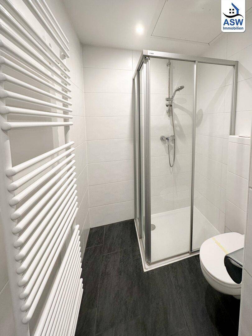 Duschbereich im modernen Badezimmer mit Glasduschkabine, WC und Handtuchheizkörper.