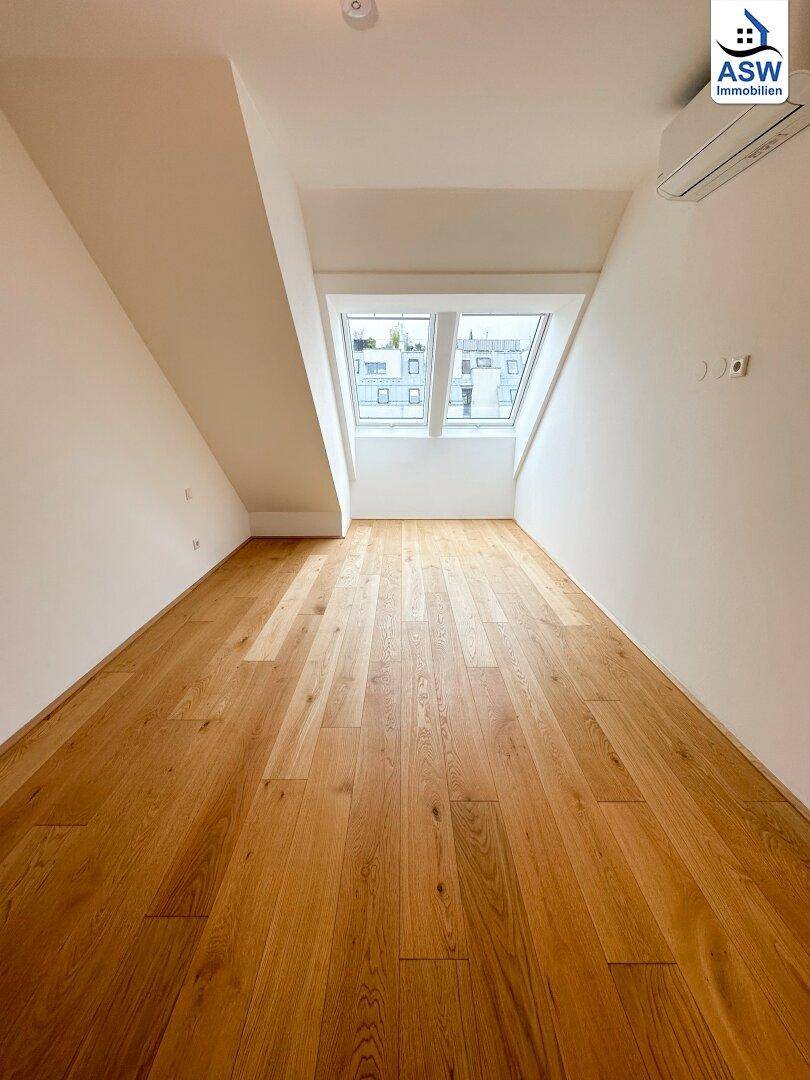 Helles Schlafzimmer im Dachgeschoss mit Holzboden, schrägen Wänden und großem Dachfenster.