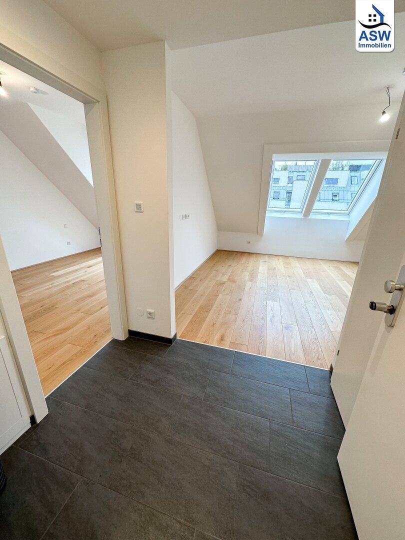Flur mit dunklen Fliesen, der zu hellen Räumen mit Holzboden im Dachgeschoss führt.