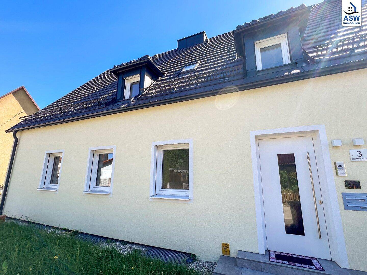 Vorderansicht eines modernen Reihenhauses mit weißer Eingangstür und großen Fenstern.