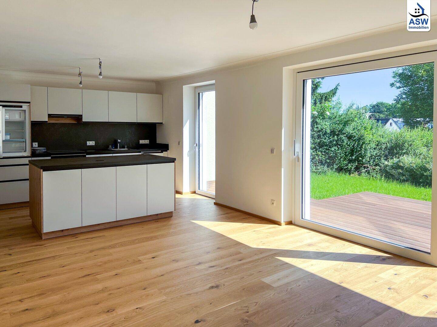 Helle, offene Küche mit Kücheninsel, Holzboden und großem Schiebefenster zum Garten.