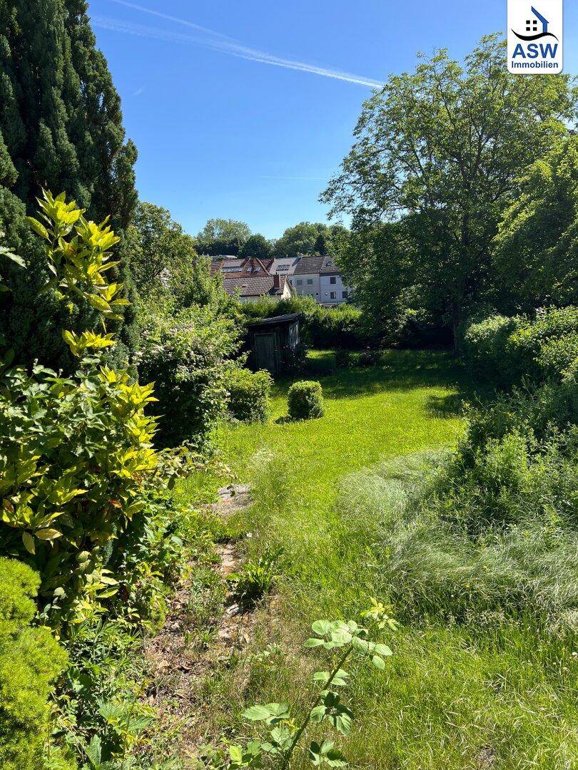 Idyllischer Gartenbereich mit üppigem Grün, hohen Bäumen und einem kleinen Gartenhaus.