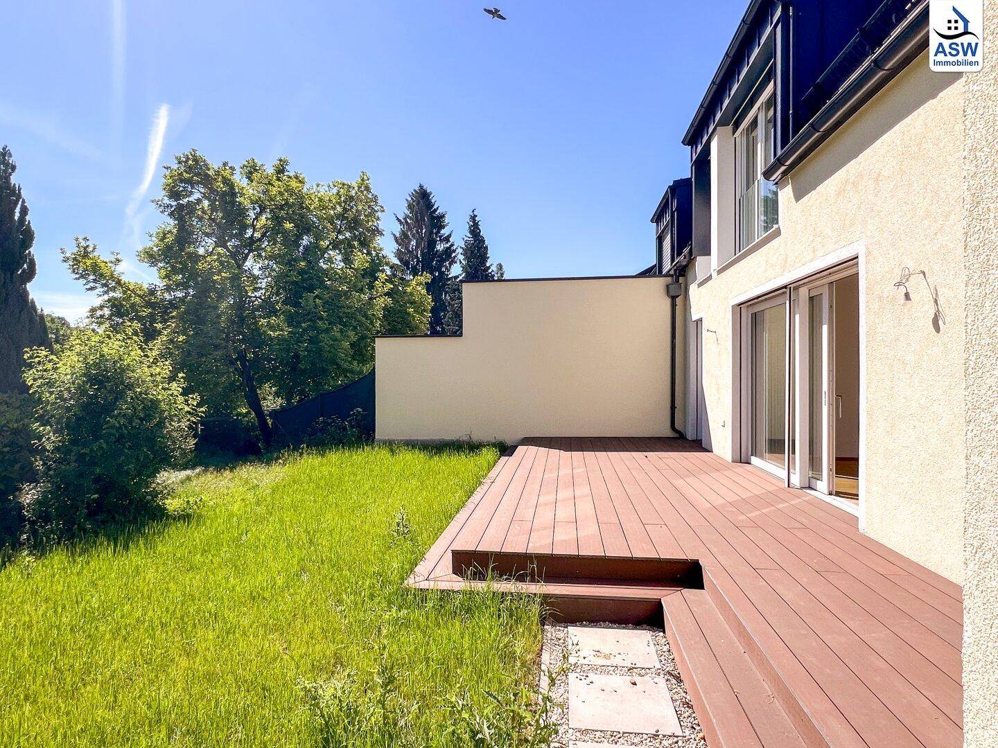 Große Holzterrasse am Haus mit Stufen zum Garten und einer hohen Sichtschutzwand.