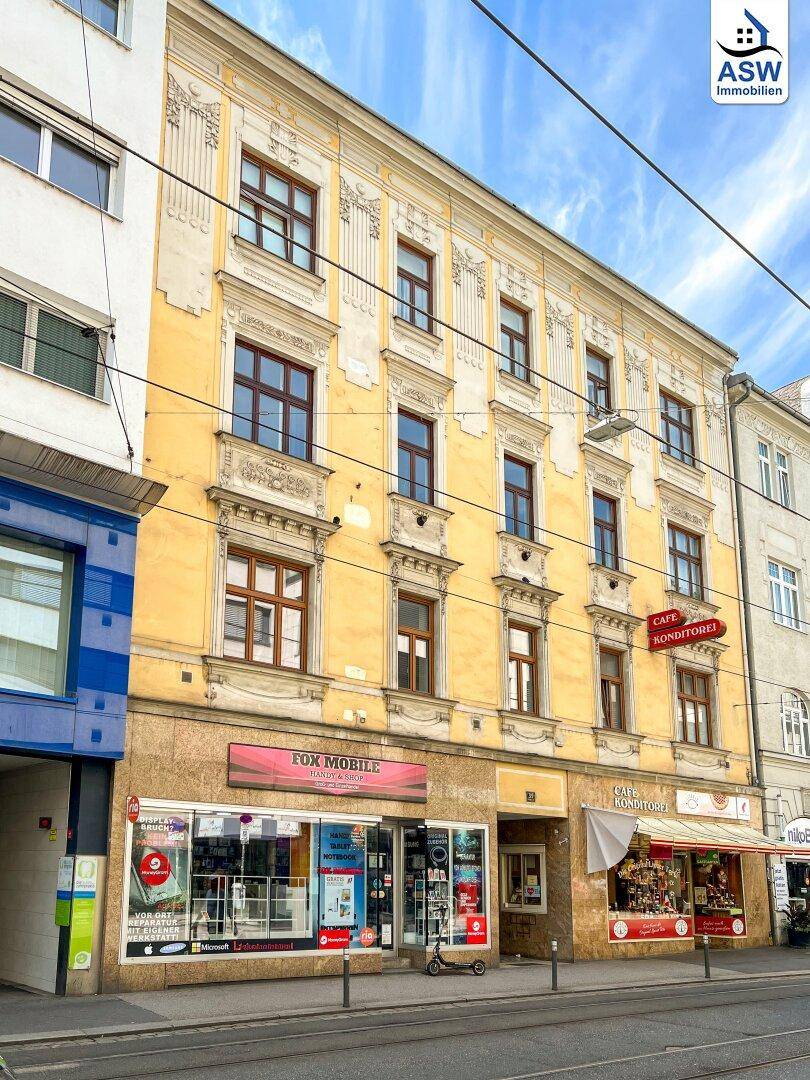 Historische Fassade eines Wohn- und Geschäftshauses mit dekorativen Elementen unter blauem Himmel.
