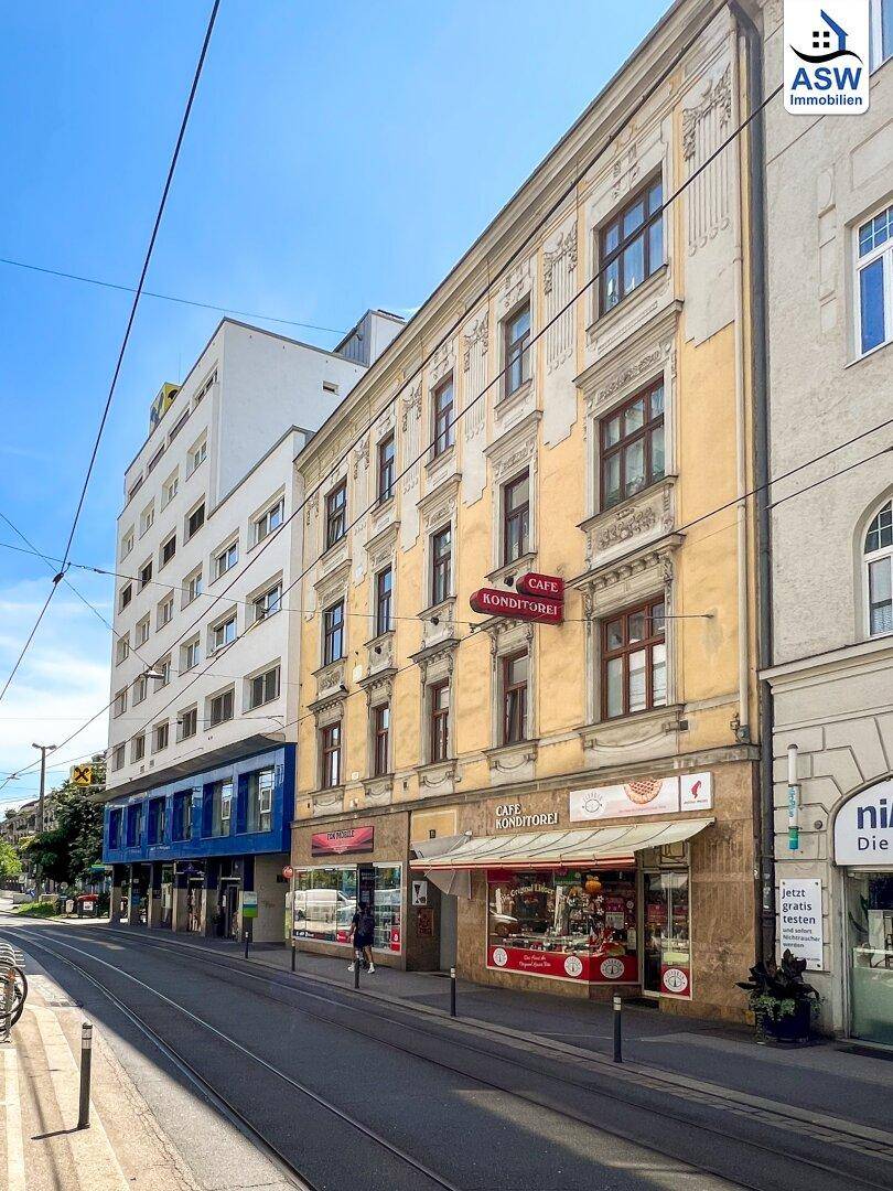 Belebtes Stadtbild mit einem historischen Gebäude und modernen Bauten entlang einer Straße mit Straßenbahnschienen.