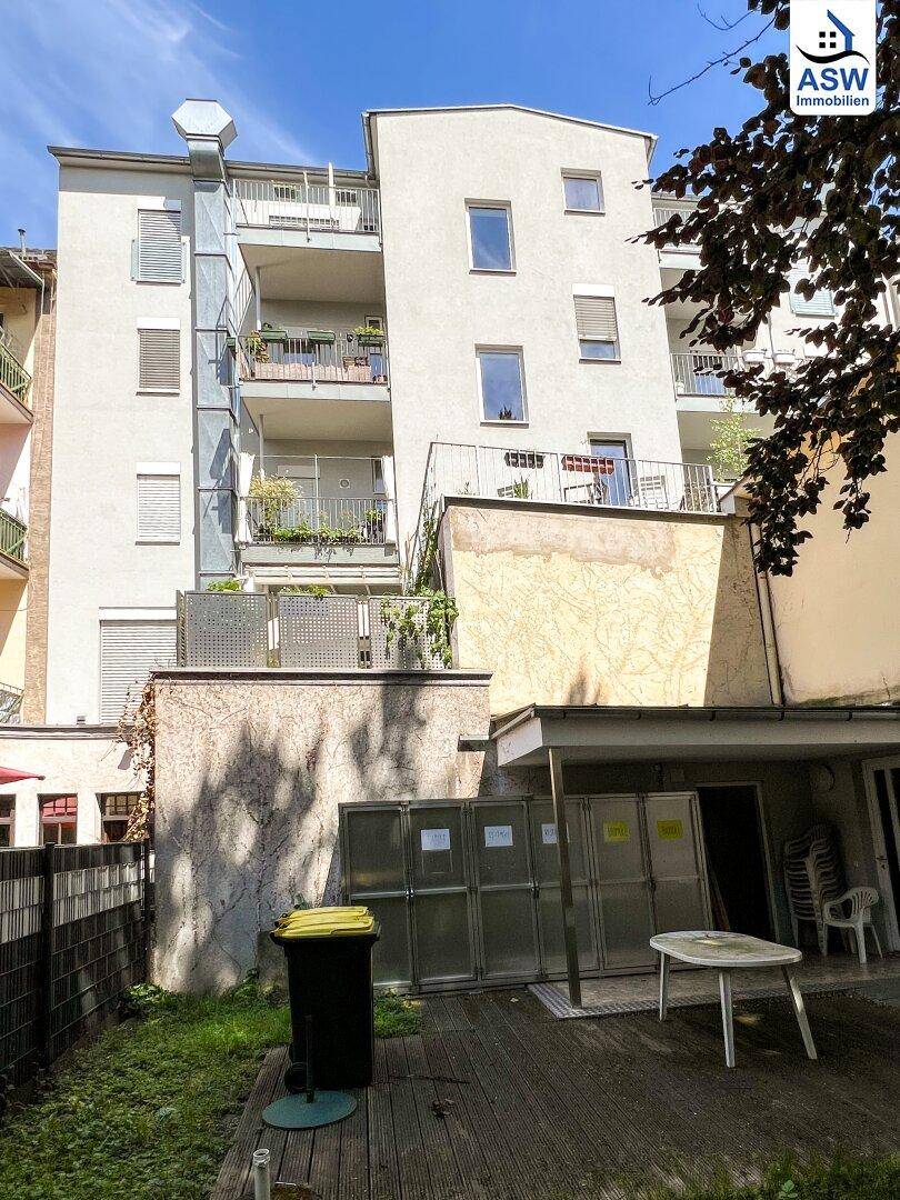 Hinterhofbereich mit einer kleinen Terrasse, Mülltonnen und Blick auf die Balkone des Wohngebäudes.