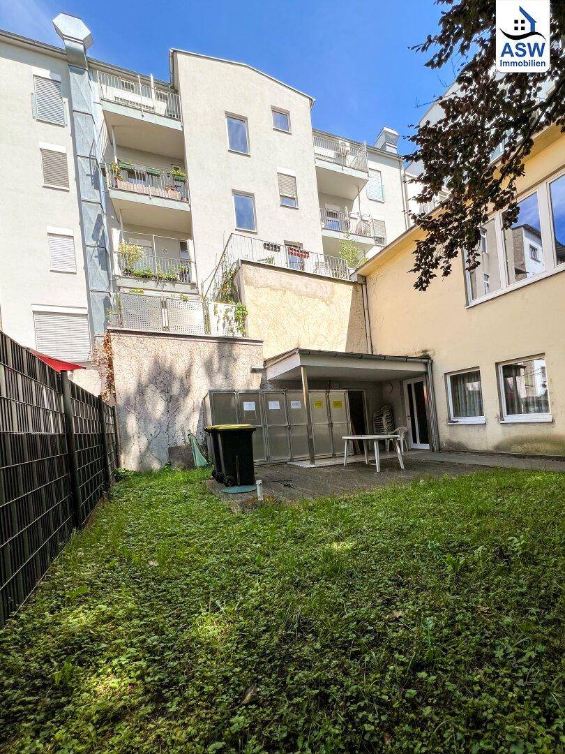 Grüner Gartenbereich hinter dem Gebäude mit einer kleinen Terrasse und Blick auf die Balkone.