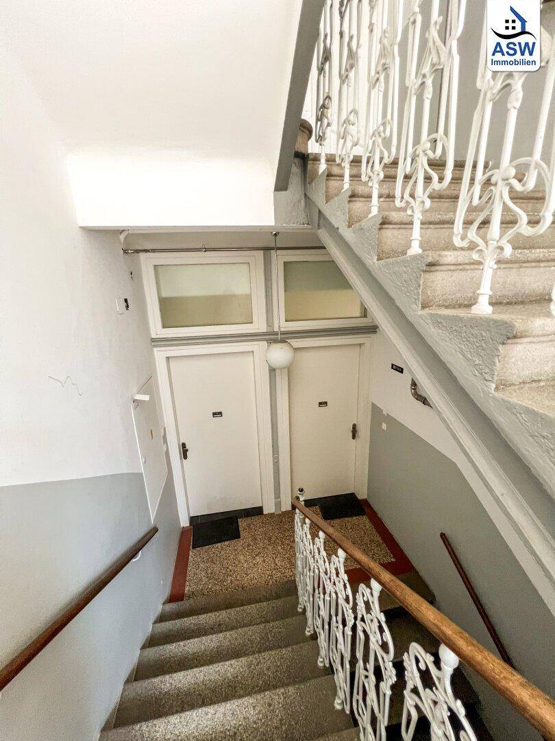 Treppenhaus in einem Altbau mit Terrazzostufen und dekorativen Geländern, führt zu Wohnungstüren.