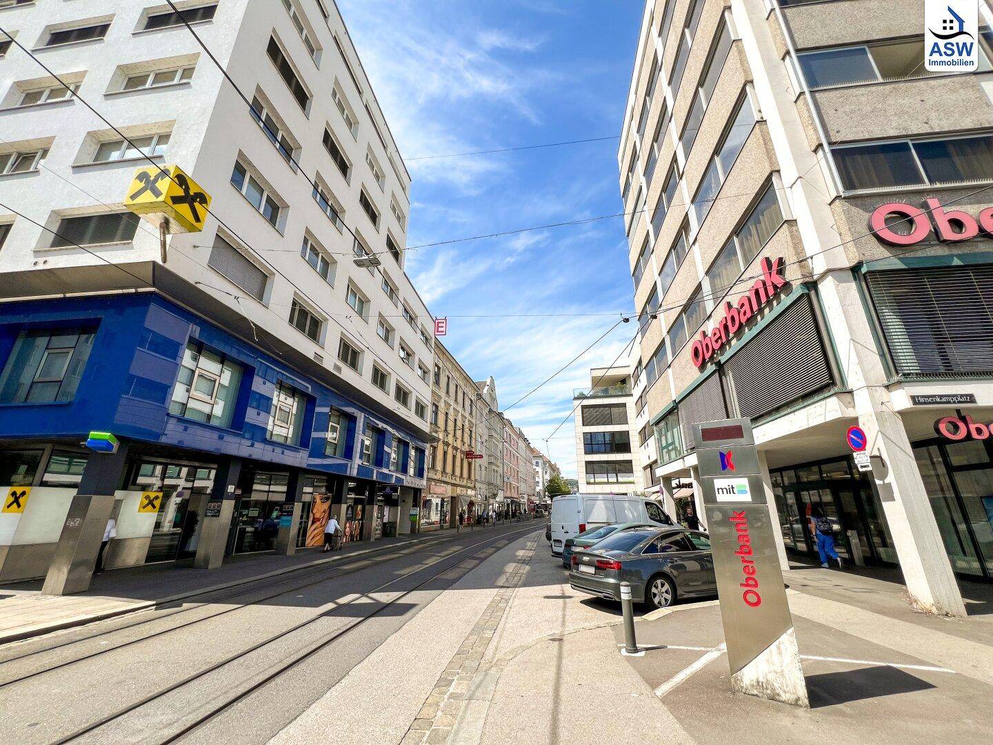 Belebtes Stadtviertel mit Geschäften, Banken und Gebäuden unter einem klaren blauen Himmel.