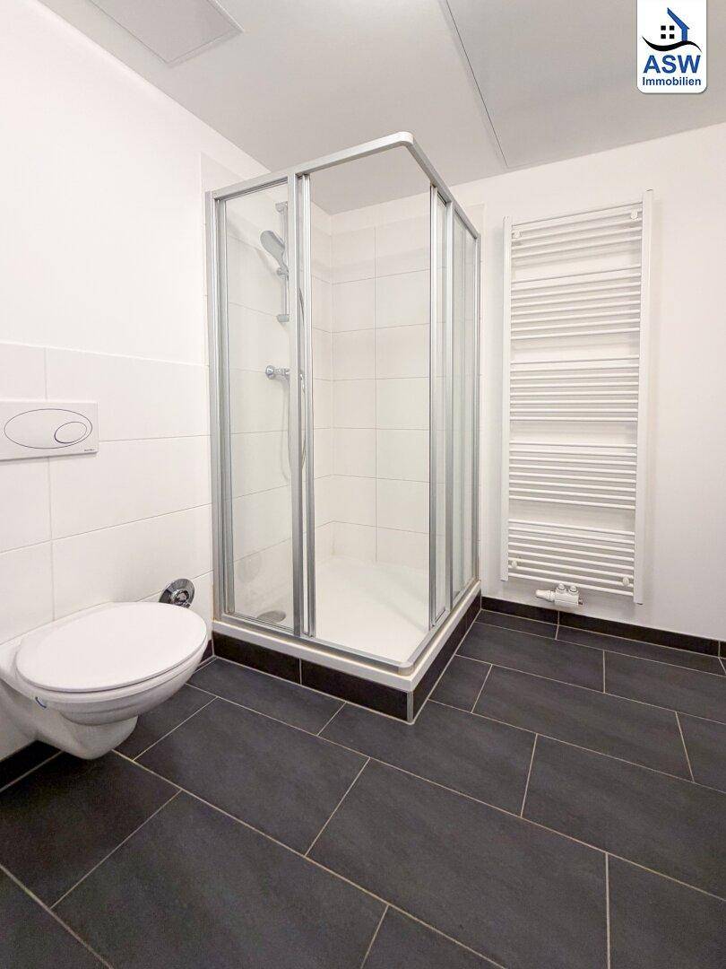 Modernes Badezimmer mit Duschkabine, Wand-WC und dunklem Fliesenboden.