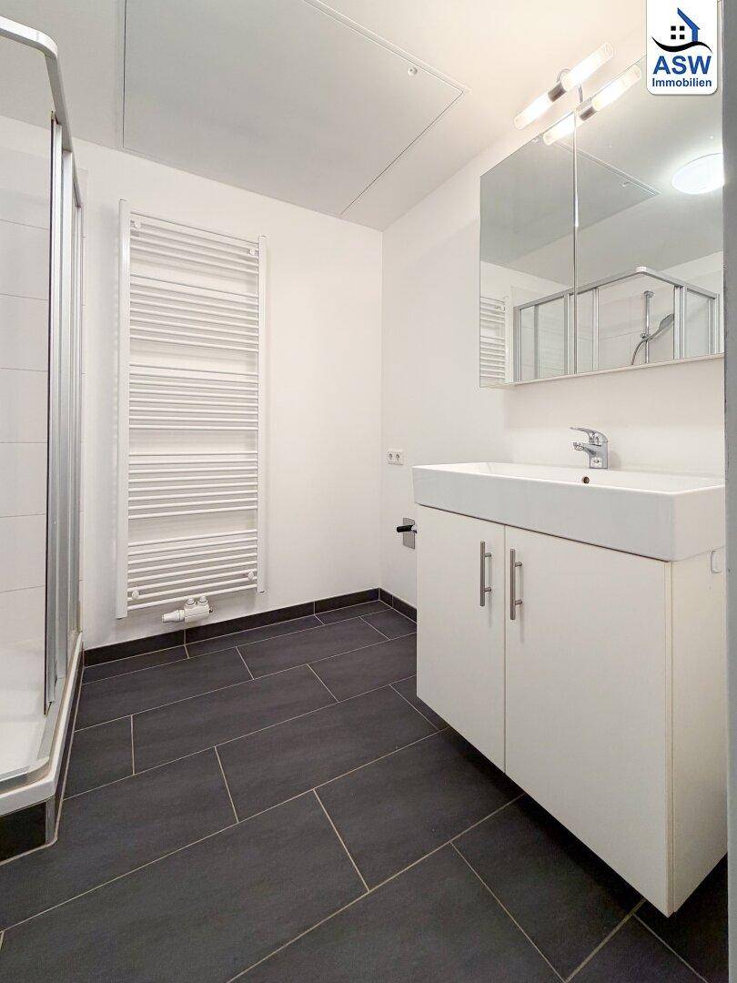 Helles Badezimmer mit modernem Waschtisch, Spiegel und Handtuchheizkörper.