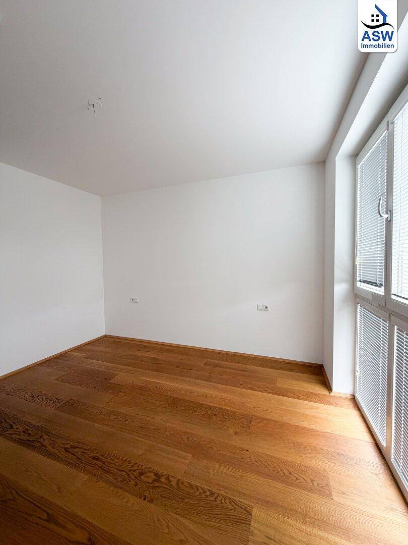 Helles Zimmer mit Parkettboden und großem Fenster, ideal als Schlaf- oder Arbeitszimmer.