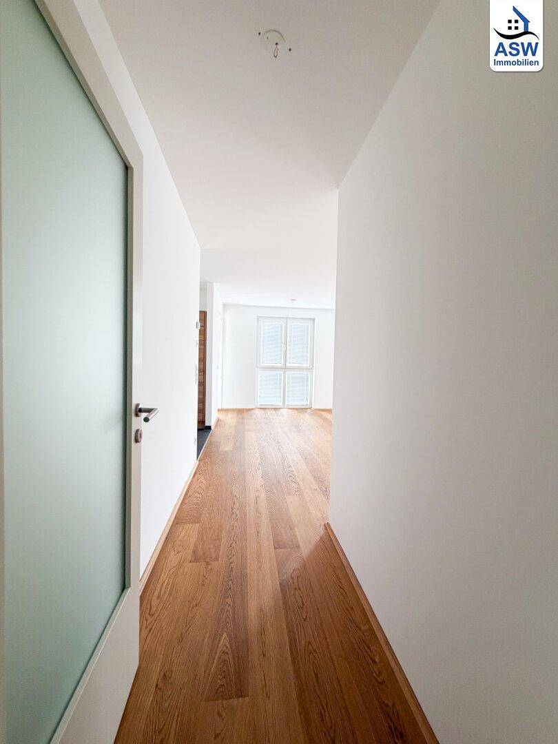 Langer, heller Flur mit Holzparkettboden, der zu weiteren Räumen führt.