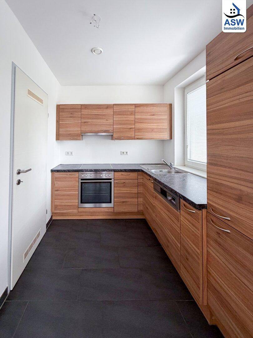 Moderne Einbauküche mit Holzfronten, dunkler Arbeitsplatte und Fliesenboden.