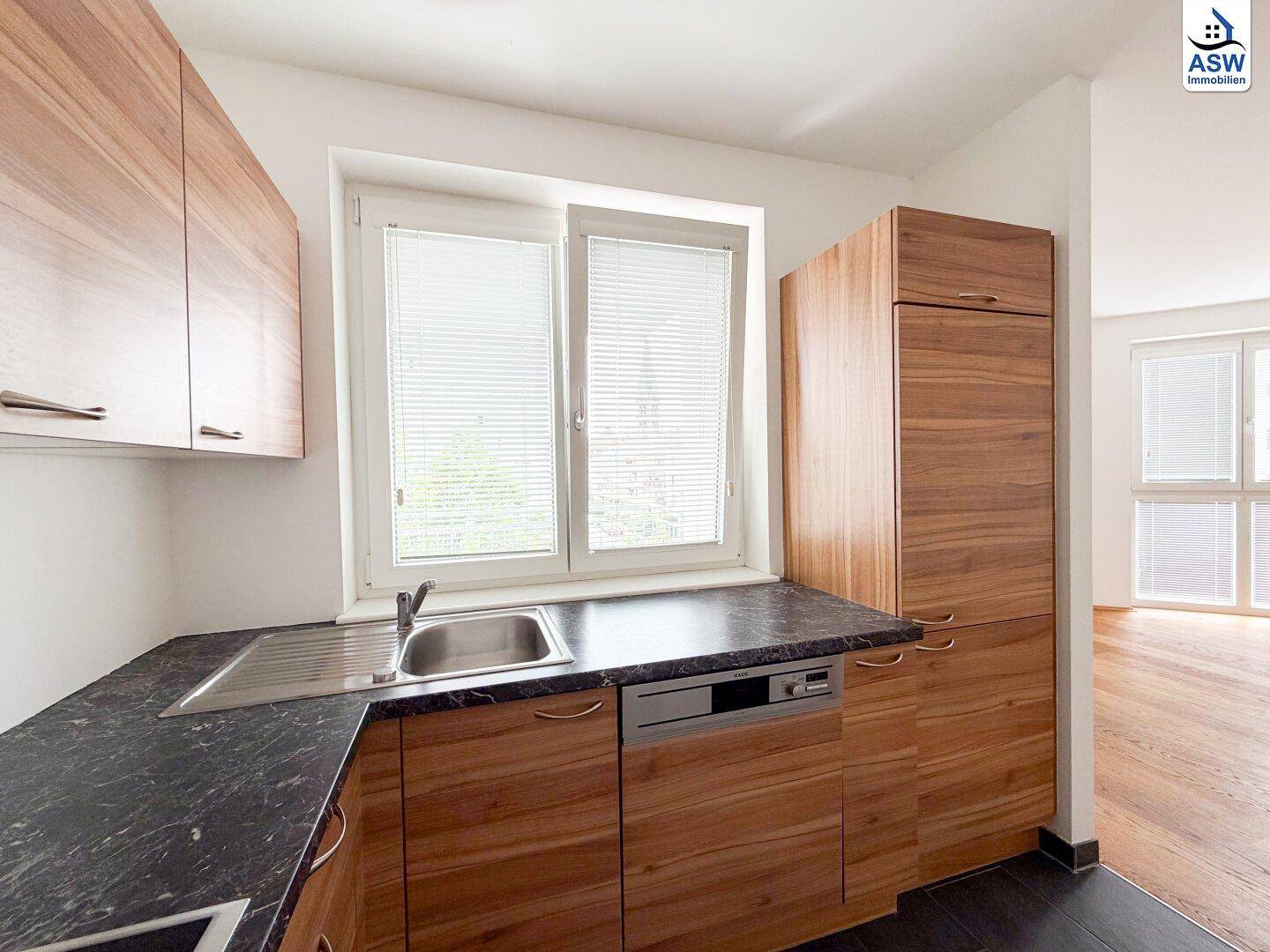 Helle Küche mit Holzschränken, Spüle und Fenster, das viel Tageslicht bietet.