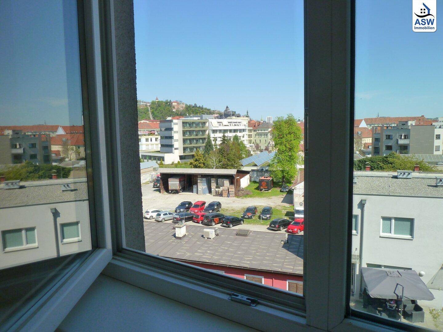 Ausblick aus dem Fenster auf eine städtische Umgebung mit Gebäuden, Parkplatz und Grünflächen.