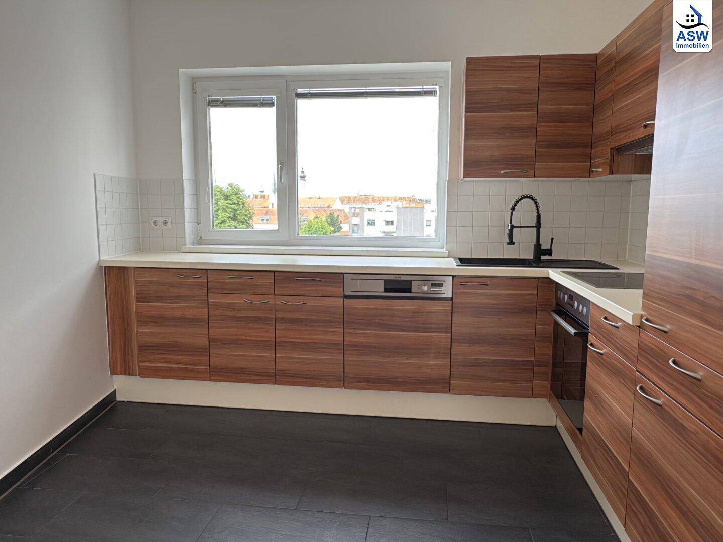 Moderne Küche mit Holzschränken, weißer Arbeitsplatte, Fliesenboden und Fenster mit Stadtblick.