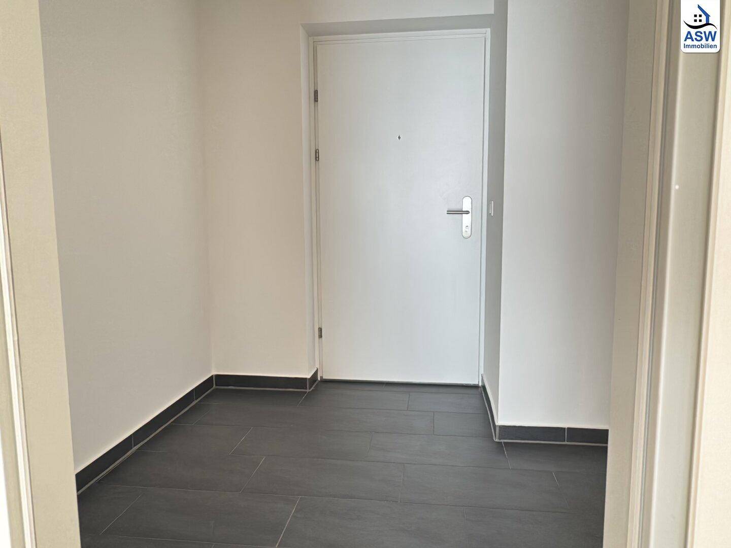 Heller Eingangsbereich mit Fliesenboden und einer schlichten weißen Eingangstür.