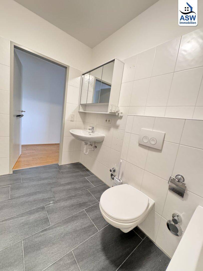 Funktionales Badezimmer mit weißen Fliesen, Toilette, Waschbecken und Spiegelschrank.