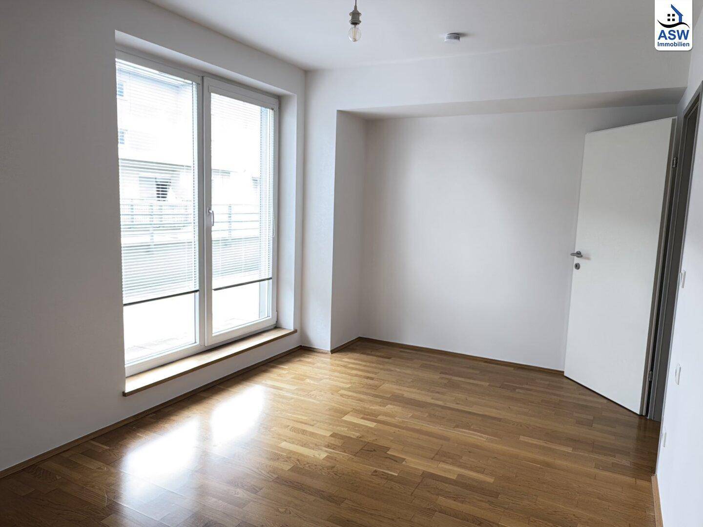 Helles Schlafzimmer mit Parkettboden, weißen Wänden und großem Fenster mit Jalousien.
