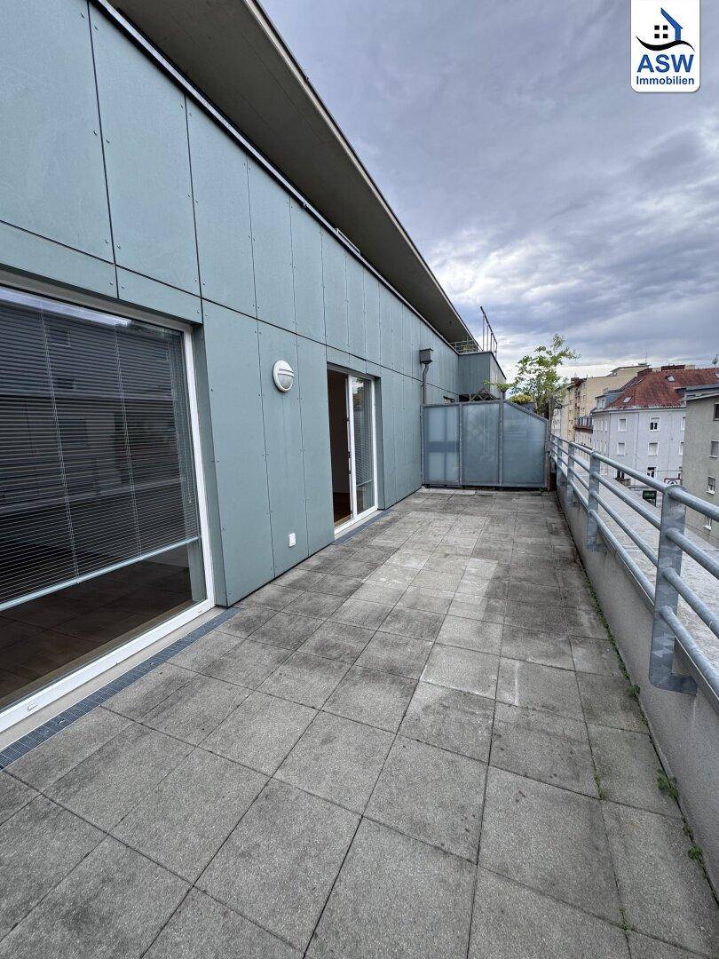 Geräumige Terrasse mit Fliesenboden und Blick auf die Stadt unter bewölktem Himmel.