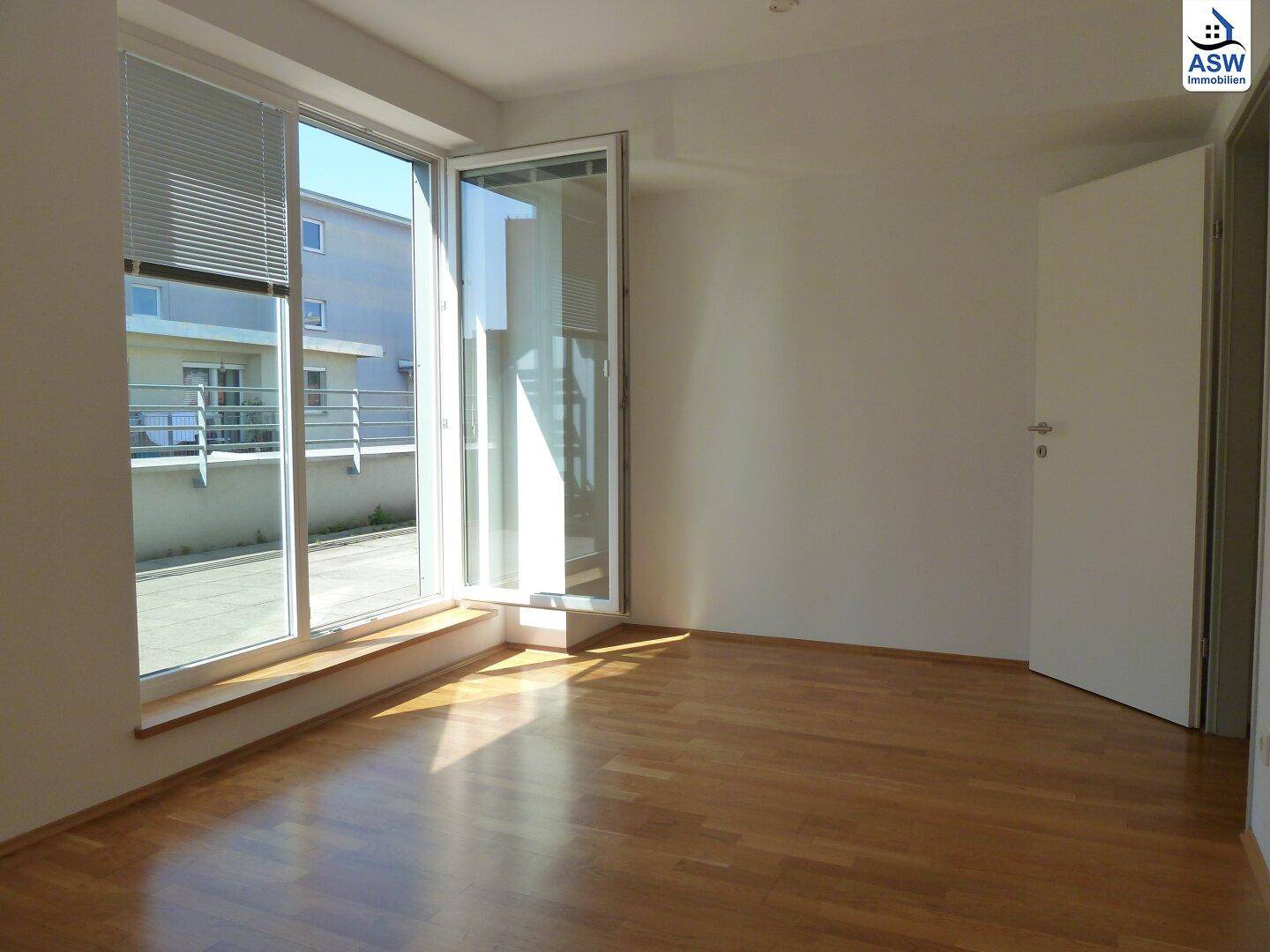 Helles Schlafzimmer mit Parkettboden und Zugang zu einem Außenbereich durch eine große Glastür.