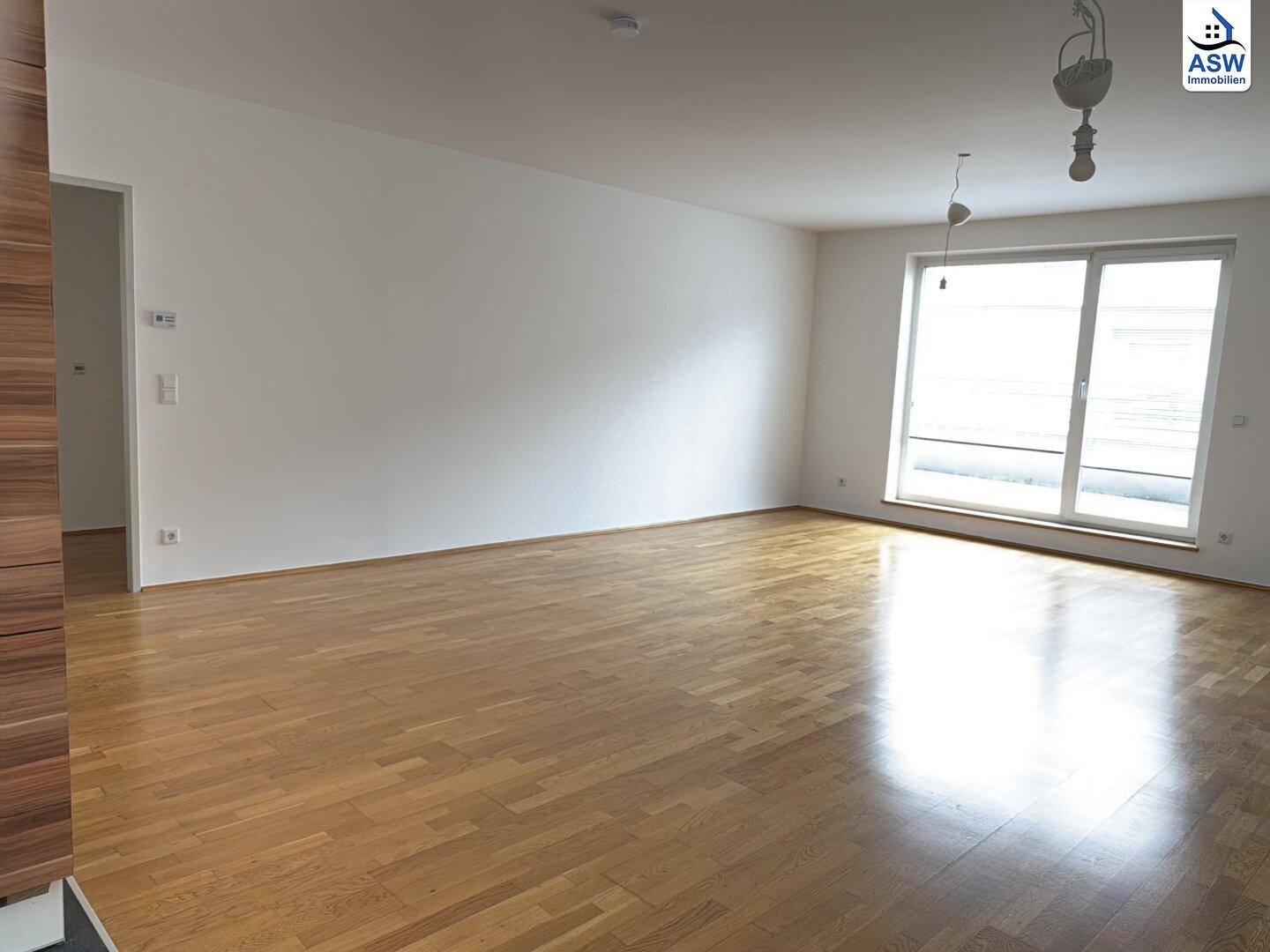 Helles Wohnzimmer mit Parkettboden, weißen Wänden und großem Fenster mit Zugang zur Terrasse.