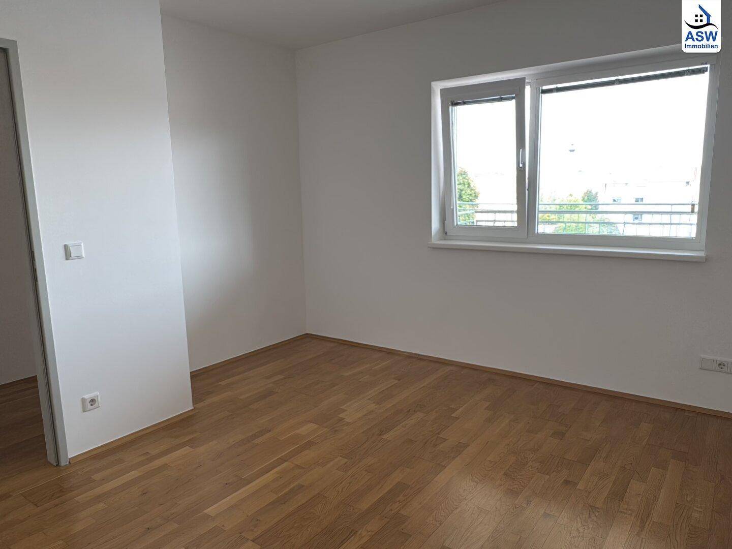 Leeres Zimmer mit hellem Parkettboden, weißen Wänden und Fenster mit Blick auf die Stadt.