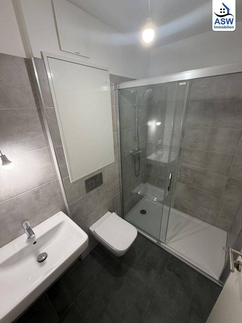 Modernes Badezimmer mit grauen Fliesen, Duschkabine und wandhängendem WC.
