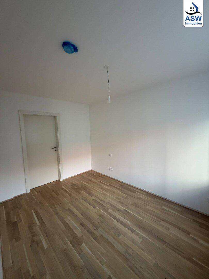 Leeres Zimmer mit hellem Parkettboden und weiß gestrichenen Wänden, bereit zum Einzug.