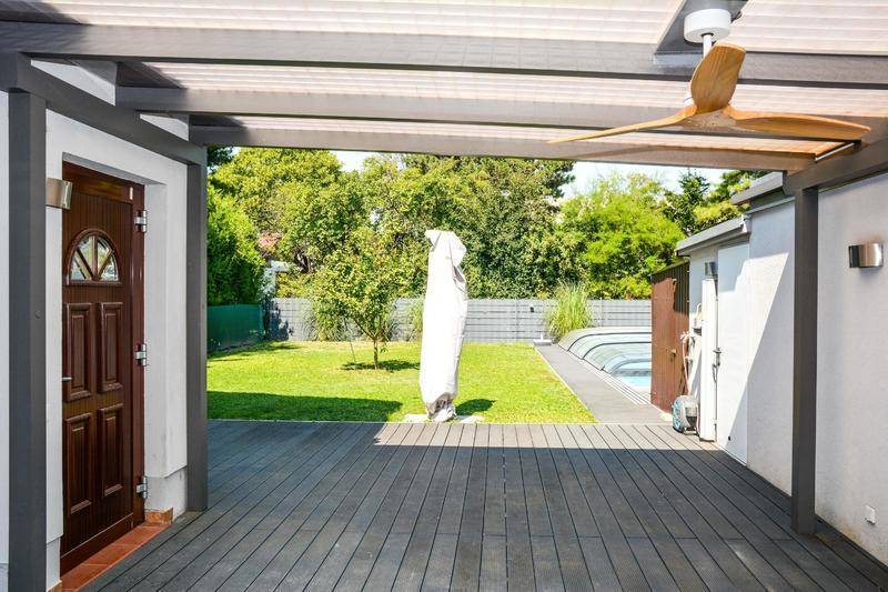 Überdachte Terrasse mit Holzoptik-Boden, Deckenventilator und Blick in den Garten mit Pool.