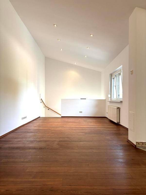 Geräumiges Wohnzimmer mit dunklem Holzboden und viel natürlichem Licht durch die Fenster.