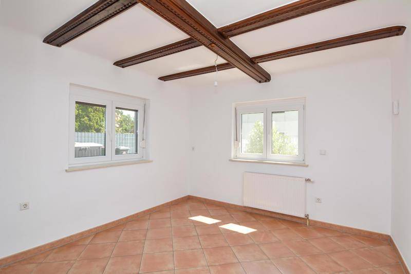 Heller Raum mit Terrakotta-Fliesen, sichtbaren Holzbalken und zwei Fenstern.