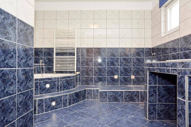 Geräumiges Badezimmer mit blauen Fliesen, Eckbadewanne und beheiztem Handtuchhalter.