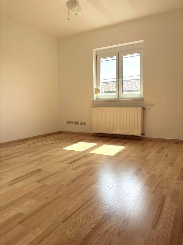 Sonniger Schlafbereich mit hellem Holzboden und großem Fenster für viel Tageslicht.
