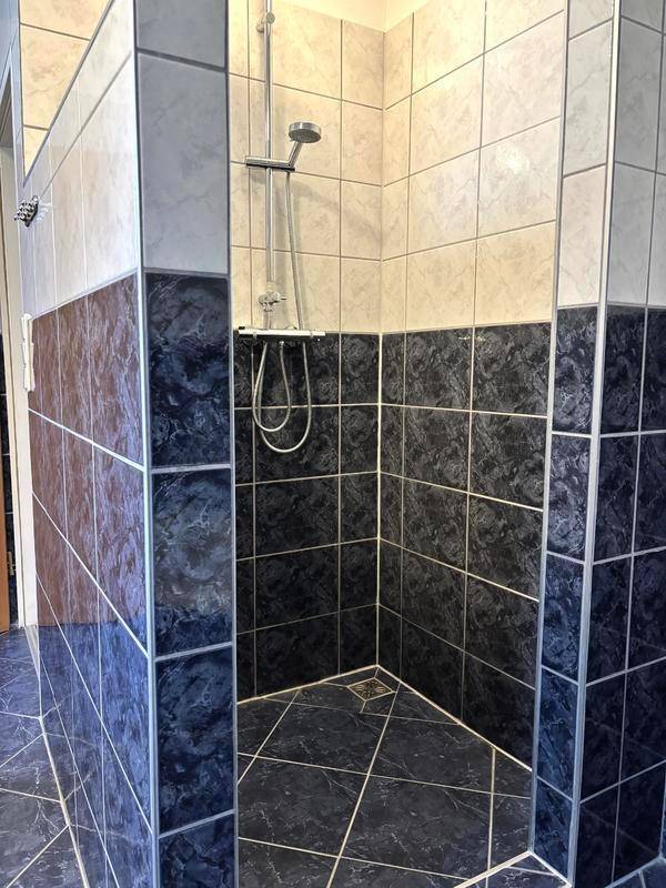 Duschbereich im Badezimmer mit dunklen und hellen Fliesen und einfacher Duscharmatur.