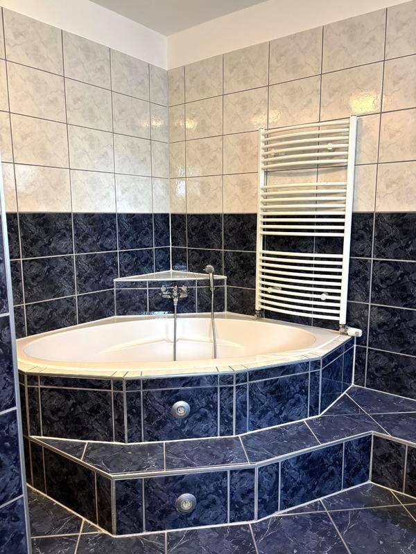 Eckbadewanne im Badezimmer mit blauen Fliesen und integrierter Beleuchtung.