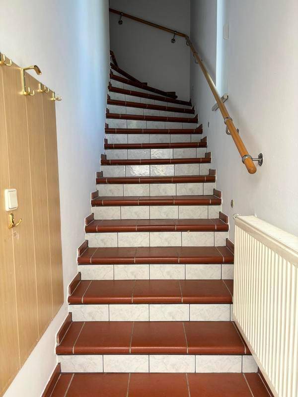 Treppenhaus mit gefliesten Stufen und Holzgeländer, das die Etagen verbindet.