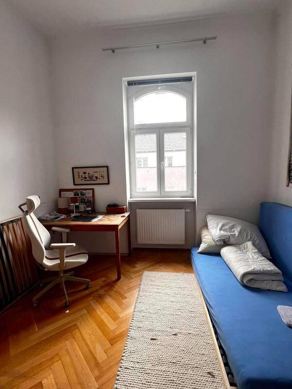 Helles Zimmer mit blauem Schlafsofa, Schreibtisch und Fischgrätparkett, ideal als Gäste- oder Arbeitszimmer.